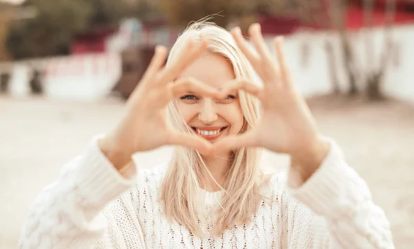 Szczęśliwy romantyczny młoda kobieta patrząc w aparat i pokazując gest serca na ulicy — Zdjęcie stockowe