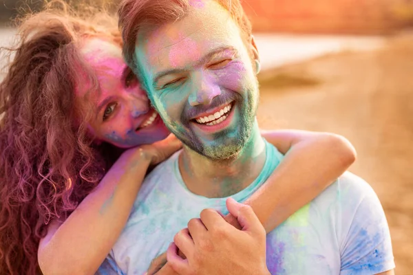 Pareja feliz con caras coloridas abrazándose en la playa — Foto de Stock