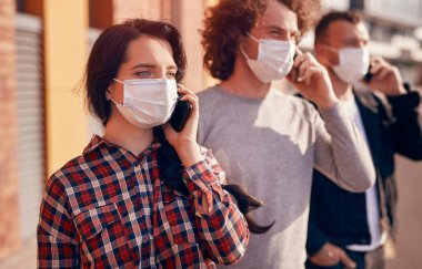 Maskeli gençler sokakta akıllı telefonlardan konuşuyor.