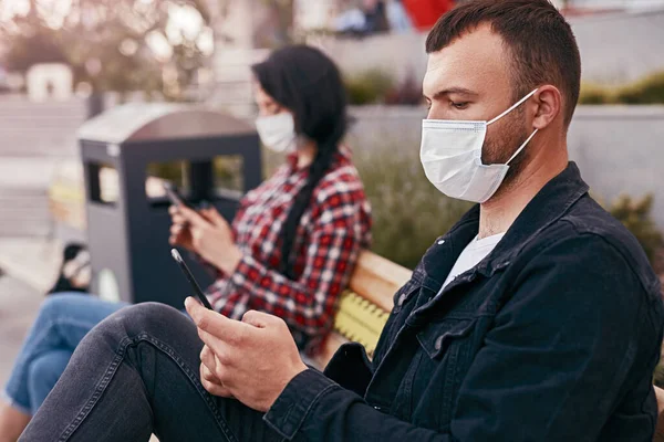 Man met masker met smartphone op bank in de buurt van vrouw — Stockfoto