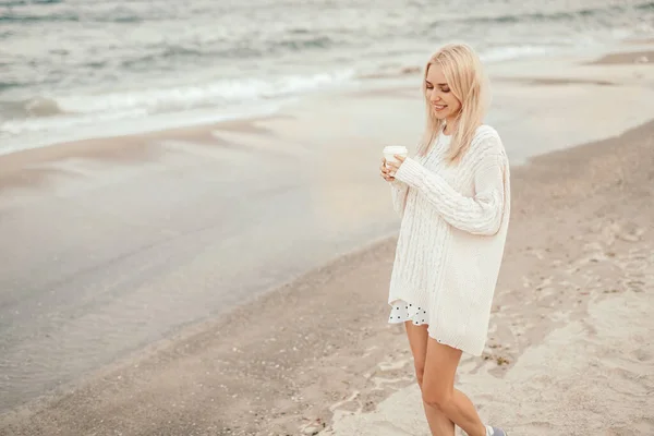 Mulher feliz com xícara de café em pé na praia de areia — Fotografia de Stock