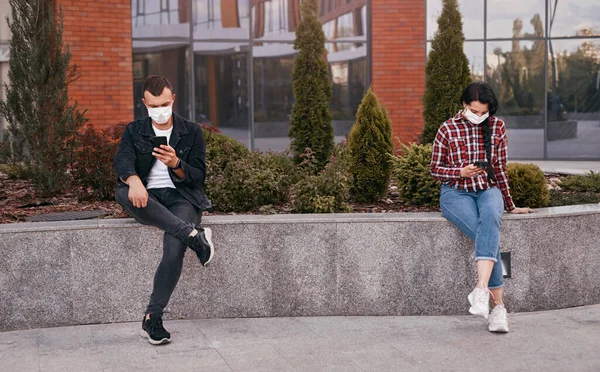 People in masks browsing smartphones on street