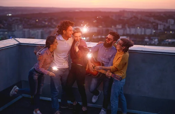 Jóvenes amigos con bengalas disfrutando de la fiesta en la azotea — Foto de Stock