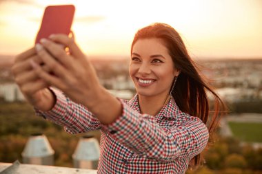 Neşeli kadın çatıdaki akıllı telefondan selfie çekiyor.