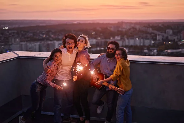 Amici felici con scintille sul tetto in serata — Foto Stock