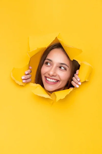 Mujer joven y feliz asomándose por el agujero en el papel — Foto de Stock