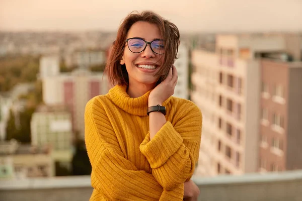 Positive young woman in warm sweater standing on rooftop — Stock Photo, Image