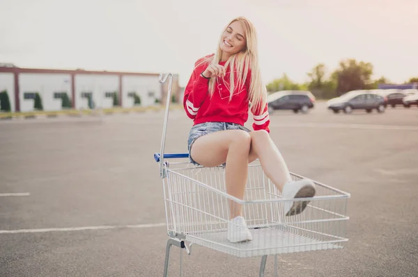 Giovane donna giocosa seduta sul carrello della spesa — Foto Stock