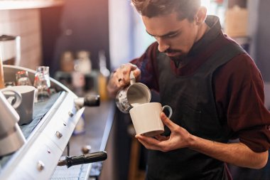 Barmen kahve bardağına süt dolduruyor.