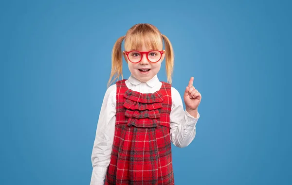 Розумна школярка в окулярах вказує вгору — стокове фото