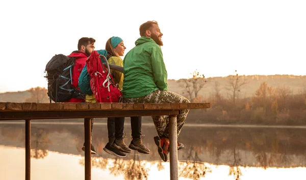 Glada resenärer med ryggsäckar vilar nära floden — Stockfoto