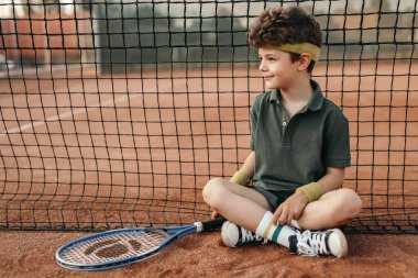 Tenis raketli çocuk kortta dinleniyor.