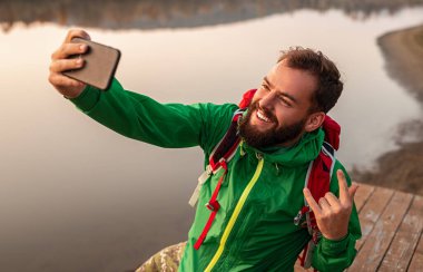 Mutlu sakallı gezgin iskelede selfie çekiyor.