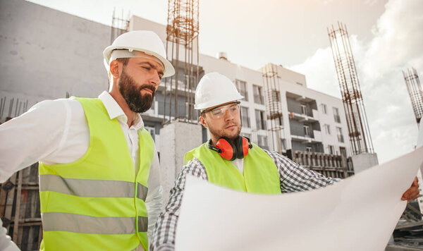 Male builders reading drafts on construction site