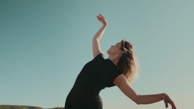 Zarif bir dansçı, açık havada açık mavi gökyüzüne doğru uzanan kollarıyla zarifçe hareket ediyor. Özgürlük, sanat ve ifade kavramı.