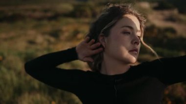 Gün batımında güneşin sıcağının tadını çıkaran bir kadının sakin, açık bir alanda yakınlaşması. Huzurlu ve rahat bir an..