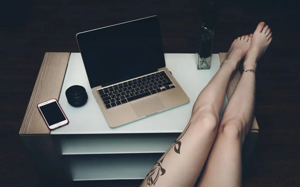 Sexy women's feet with tattoos on the table with laptop.