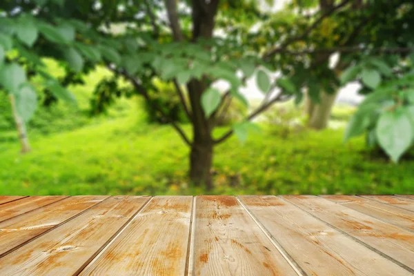 wooden tabletop against the blurred green of a leaning tree. Wooden table in the park among the trees on a summer day. Blank for design.