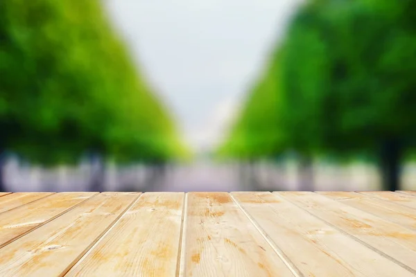 wooden tabletop against the background of blurred greenery of trees stretching into the distance. Wooden table in the park among the trees on a summer day. Blank for design.