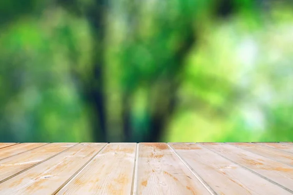 Wooden tabletop against the background of blurred green. Wooden table in the park among the trees on a summer day. Blank for design