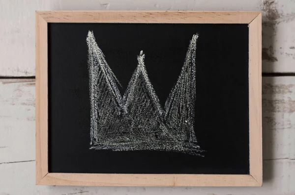 A crown drawn on small blackboard. Wealth and authority symbol