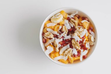 Taze meyve bir kase: mango, muz, mandalina, nar taneleri, Hindistan cevizi pul, ceviz ve kuru kayısı. Sağlıklı salata