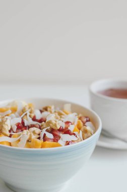 Dikey fotoğraf mavi bir kase ve hibiscus çay beyaz fincan taze meyve salatası. Sağlıklı tatlı: mango, Hindistan cevizi, nar, mandalina, muz ve sıcak bir içecek ile ceviz