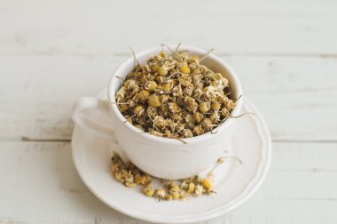 Ahşap masa üzerinde bir beyaz çay fincan kurutulmuş papatya çiçeği. Bitkisel çay