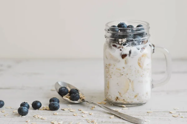Ahşap masa üzerinde bir kaşıkla gecede yulaf tam tahıl gevreği, taze bluberries ve Hindistan cevizi sütü ile servis. Kahvaltı için sağlıklı tatlı