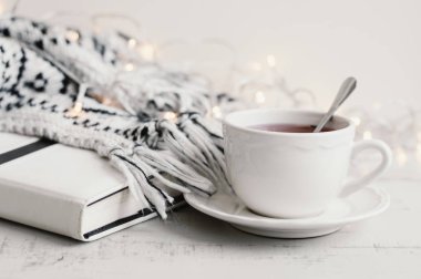 Bir fincan çay, kitap, ışıklar ve ahşap masa üzerinde örme battaniye. Çay molası, sakin ol ve kavram okuma. 