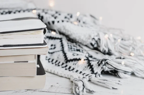Yün Battaniye, ev dekorasyonu için ışıkları ve bir yığın kitap, Günlükler ve ahşap masa üzerinde planlamacıları ördü. Okuma kavramı. Rahat ve konforlu bir atmosfer