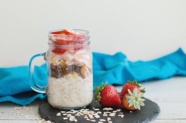 Kahvaltı tarifi: çilek ile gece yulaf servis arka plan olarak siyah arduvaz kurulu, mavi peçeteye. Sağlıklı beslenme