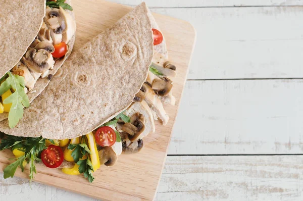 Healthy and balanced meal: whole wheat wrap with chicken breast, sliced mushroom, cherry tomato, yellow bell pepper, arugula and parsley