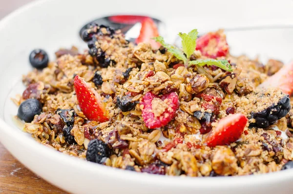 Ev yapımı granola bal, tohum, kurutulmuş meyve, fındık ve taze çilek ile beyaz bir kase içinde servis. Tatlı kahvaltı