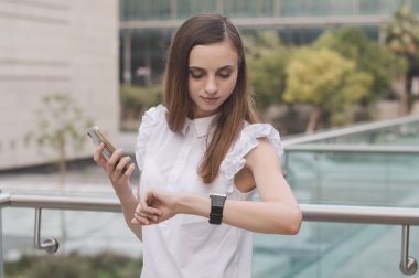 Avrupa kadın kahverengi saçlı ve beyaz iş bakmak bir cep telefonu tutan bluz ve el altında seyir izliyor. Zaman yönetimi kavramı. Genç iş kadın ya da erkek girişimci