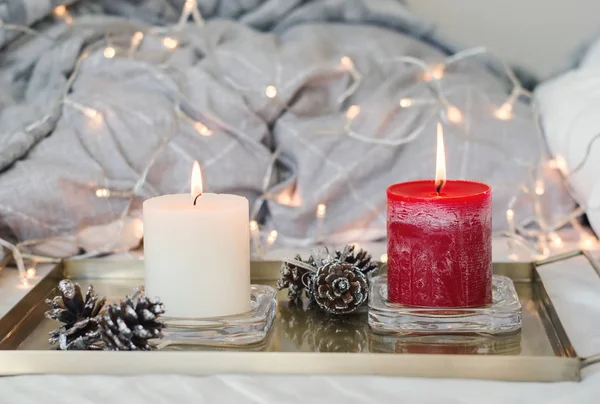 Beyaz ve kırmızı renkli ve dekoratif kozalaklar, ışıklar arka plan olarak iki mum ile altın metal tepsi. Yatak odası dekor. Hygge tarzı