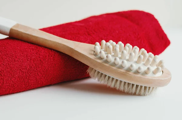 Wooden brush for dry body massage and red cotton towel on white background. Cellulite treatment. Self massage tool