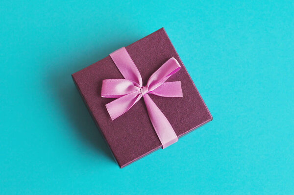 Small purple gift box with pink ribbon on turquoise background. Present for anniversary, birthday, New Year, Christmas