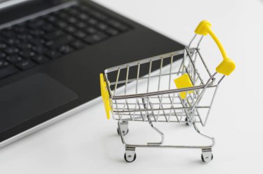 Beyaz masada küçük alışveriş sepeti oyuncak ve bilgisayar. Online alışveriş konsepti. E-ticaret