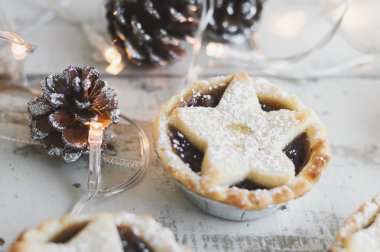 Ahşap masa ve dekoratif çam kozalağı ve Noel ışıkları üzerinde kıyma pasta. Yeni yıl ve Noel kutlamaları. Noel tatlısı
