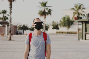 Gri tişörtlü, güneş gözlüklü ve siyah koruyucu maskeli genç bir adam. Sosyal uzaklık ve yeni norm kavramı