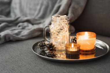 Oturma odası dekoru: iki yanan turuncu aroma mumu, çam kozalakları ve cam kavanozda noel ışıkları. Hygge konsepti. Sonbahar - Kış mevsimi