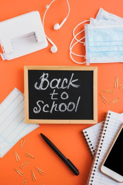 Coronavirüs salgını sırasında okula döndüm. Turuncu zemin üzerinde okul kırtasiyesi olan dikey Düz