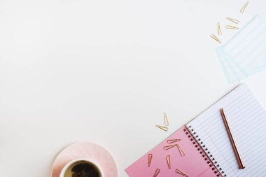 Boş sayfaları, metal kalemleri, çıkartmaları, ataçları ve pembe bardakta yeşil çayları olan pembe defterli bir daire.