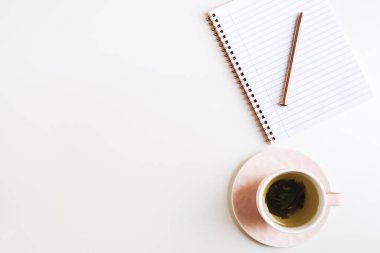 Pembe fincanlarda yeşil çay, boş sayfalı not defteri ve beyaz masada metal kalem, metin için boşluk.