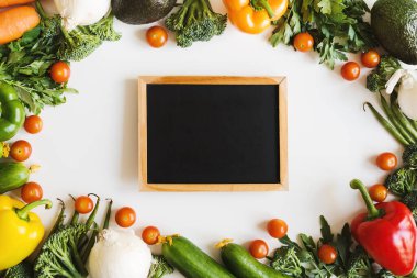 Boş karatahta ve beyaz arka planda taze mevsimlik sebzelerden oluşan çerçeve, üst manzara, yazı için alan. Sağlıklı beslenme. Yerel gıda konsepti