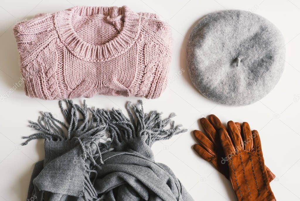 Handmade knitted sweater, gray scarf, beret hat, suede gloves on white background, top view. Winter and autumn warm clothes. Wardrobe essentials 