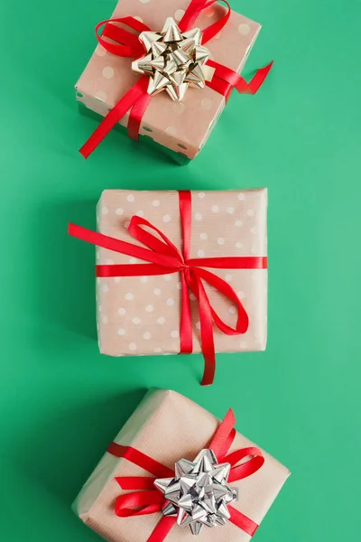 三个礼品盒用手工纸包着红色缎带和绿色背景的金色和银色蝴蝶结 俯瞰全景 圣诞礼物平放 — 图库照片