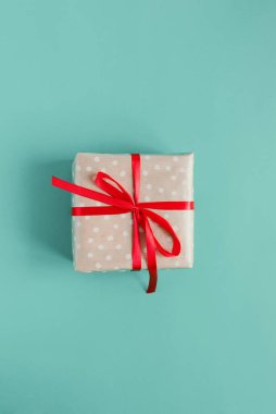 El işi polka kağıdına sarılı küçük bir hediye kutusu ve mavi arka planda kırmızı kurdele. Çevre dostu Noel paketleme fikri