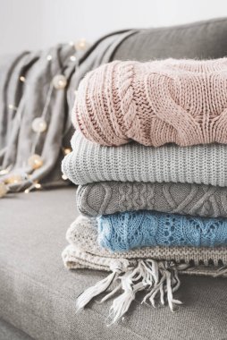 Gri kanepe yatağında örülmüş süveter yığını. Soğuk hava için el yapımı kazaklar. Örgü bakım ve depolama konsepti